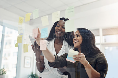 Buy stock photo Cropped shot of two attractive young businesswomen standing together and using a glass board to brainstorm in the office