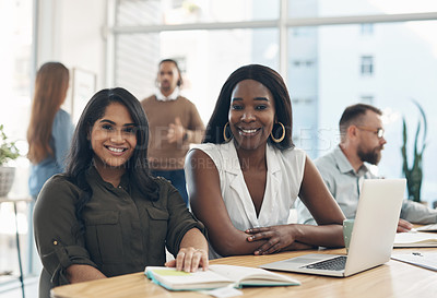Buy stock photo Cropped portrait of two young businesswomen sitting together and using a laptop while their colleagues work in the background