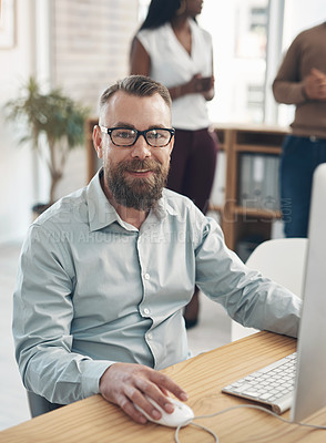 Buy stock photo Cropped portrait of a handsome young businessman sitting and using a computer while his colleagues work in the background