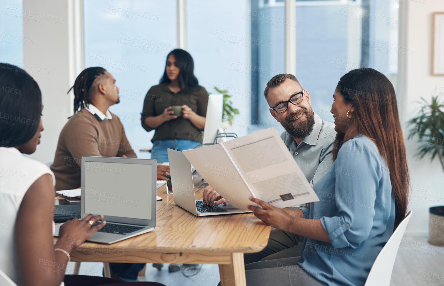 Buy stock photo Cropped shot of two young businesspeople sitting together and reading through paperwork while their colleagues work in the background