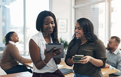 Buy stock photo Cropped shot of two attractive businesswomen using a tablet in the office while their colleagues work behind them