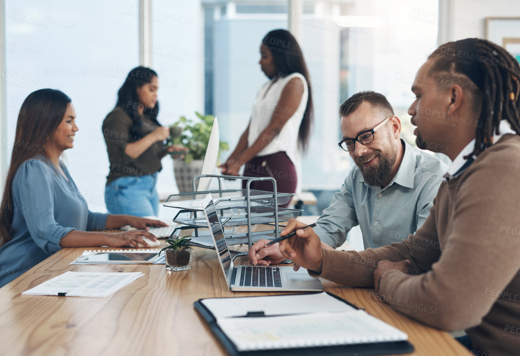 Buy stock photo Cropped shot of two handsome businessmen sitting and using a laptop in the office while their colleagues work around them