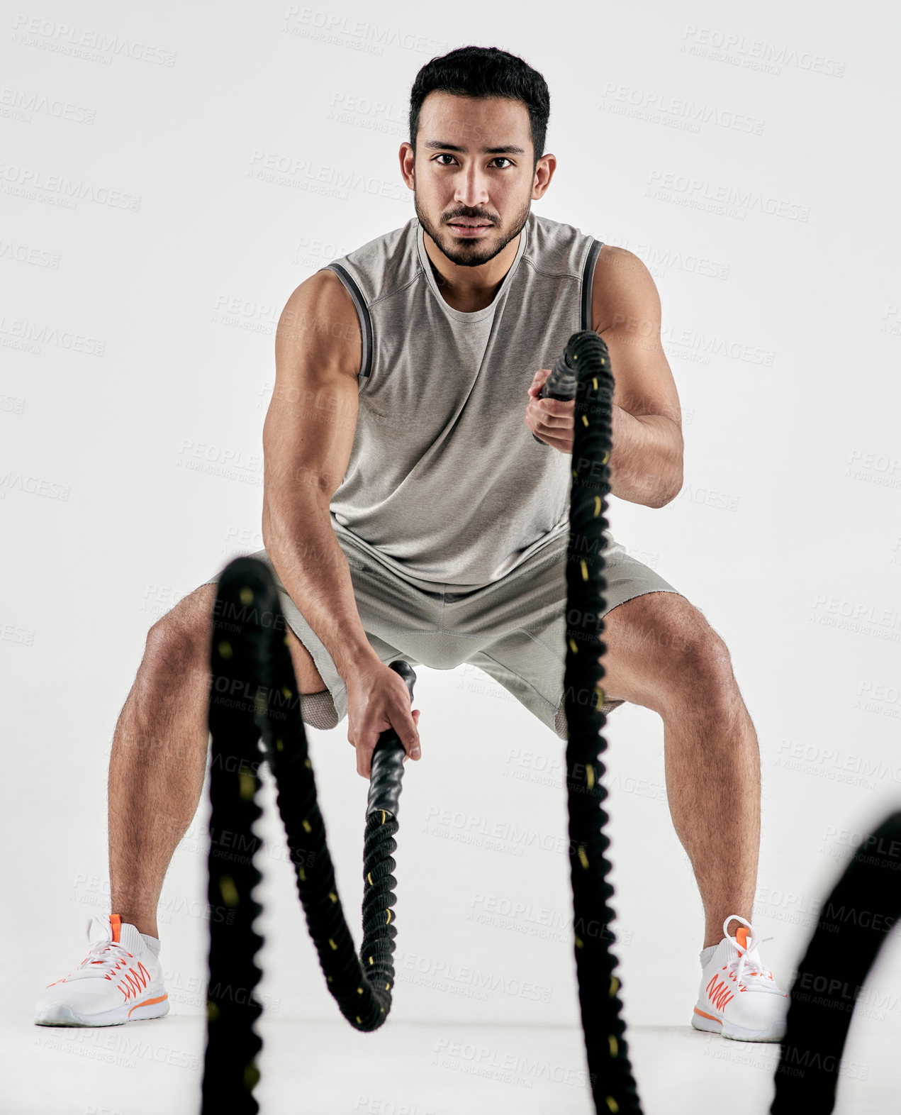 Buy stock photo Studio portrait of a muscular young man exercising with battle ropes against a white background