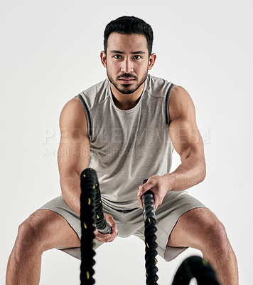 Buy stock photo Studio portrait of a muscular young man exercising with battle ropes against a white background