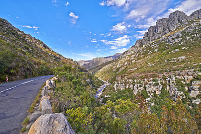 Buy stock photo Empty road in the mountains with a cloudy blue sky. Landscape of a countryside roadway for traveling on a mountain pass along a beautiful scenic nature drive with greenery and views of rolling hills