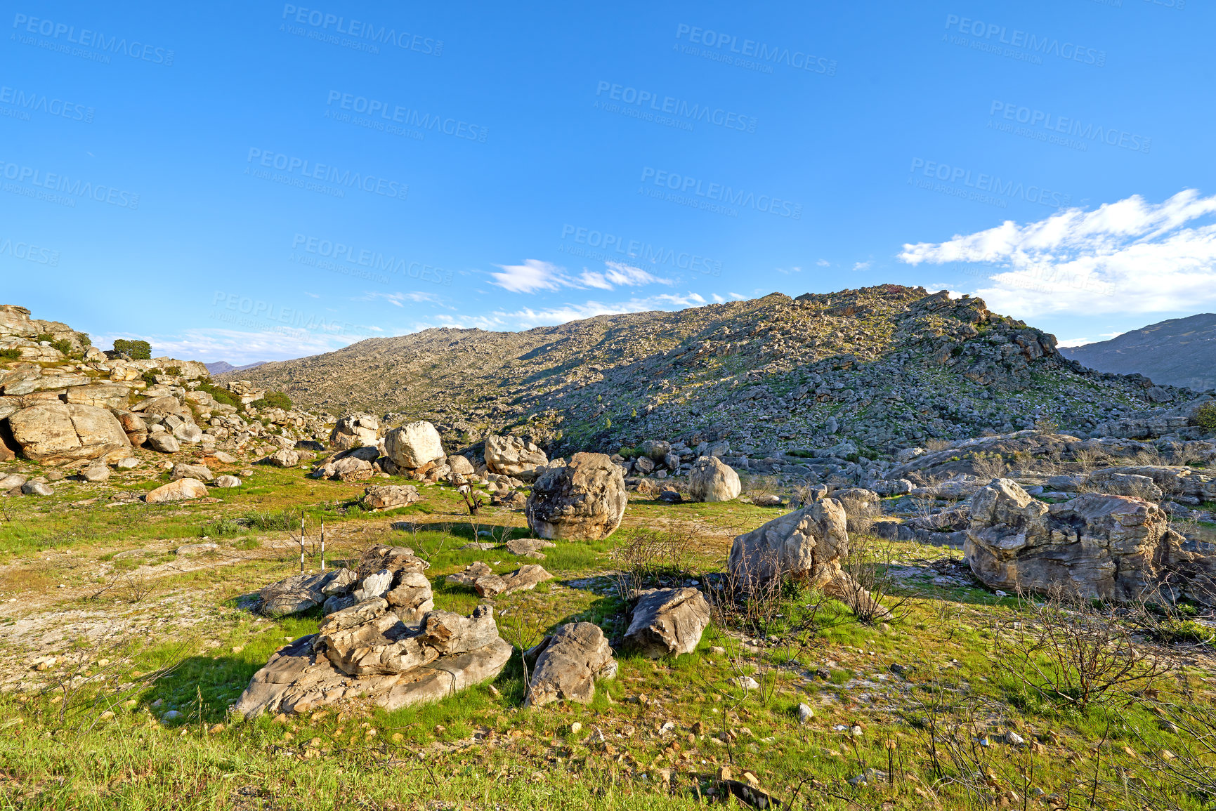 Buy stock photo A rocky mountainside landscape with green lush grass growing in an ecological rural environment. Beautiful field on rough terrain in nature with a scenic blue sky in the Western Cape during summer