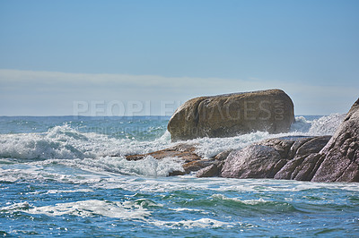 Buy stock photo Copy space of a turbulent sea with rough tides and choppy waves from strong winds crashing onto big boulders at the beach with a clear blue sky background. Rocky coast in Camps Bay, South Africa