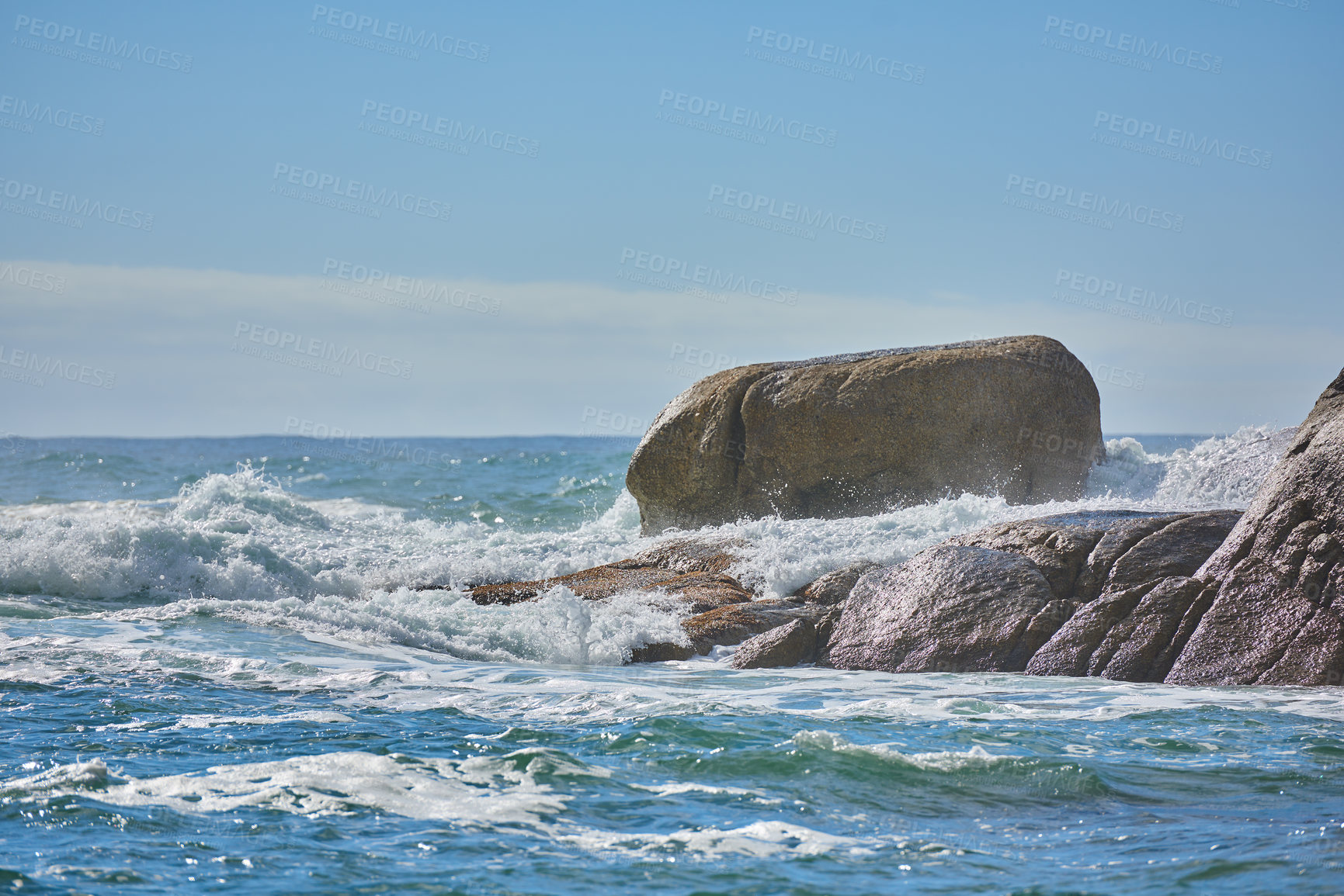 Buy stock photo Copy space of a turbulent sea with rough tides and choppy waves from strong winds crashing onto big boulders at the beach with a clear blue sky background. Rocky coast in Camps Bay, South Africa