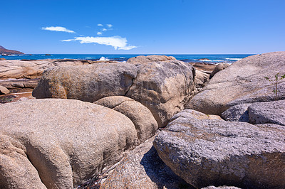 Buy stock photo Rocky coastline with the ocean and blue sky with copyspcae in the background. Stunning nature landscape or seascape of rocks. Boulders or big natural stones in the sea with beautiful rough textures