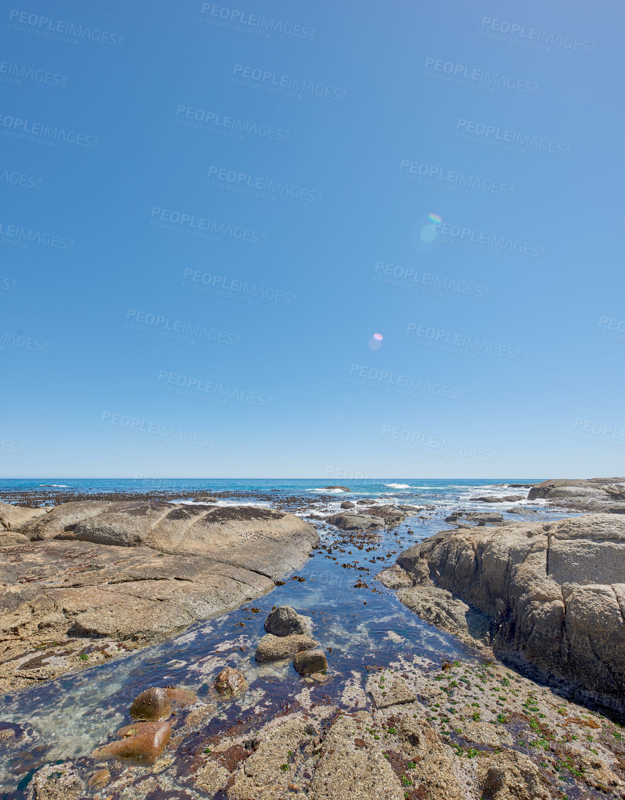 Buy stock photo Copy space at sea with a clear blue sky background and rocky coast in Camps Bay, Cape Town, South Africa. Boulders at a beach shore across a majestic ocean. Scenic landscape for a summer holiday