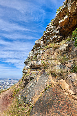 Buy stock photo A rocky mountain with plants and shrubs growing against a cloudy sky background with copy space. Rugged, remote and quiet landscape with rocks and stones on a cliff to explore during scenic hiking