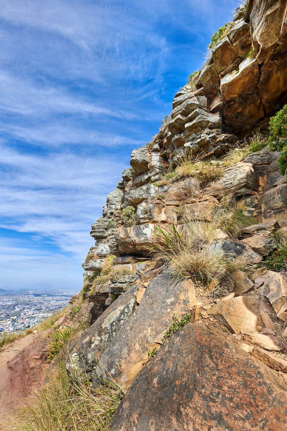 Buy stock photo A rocky mountain with plants and shrubs growing against a cloudy sky background with copy space. Rugged, remote and quiet landscape with rocks and stones on a cliff to explore during scenic hiking