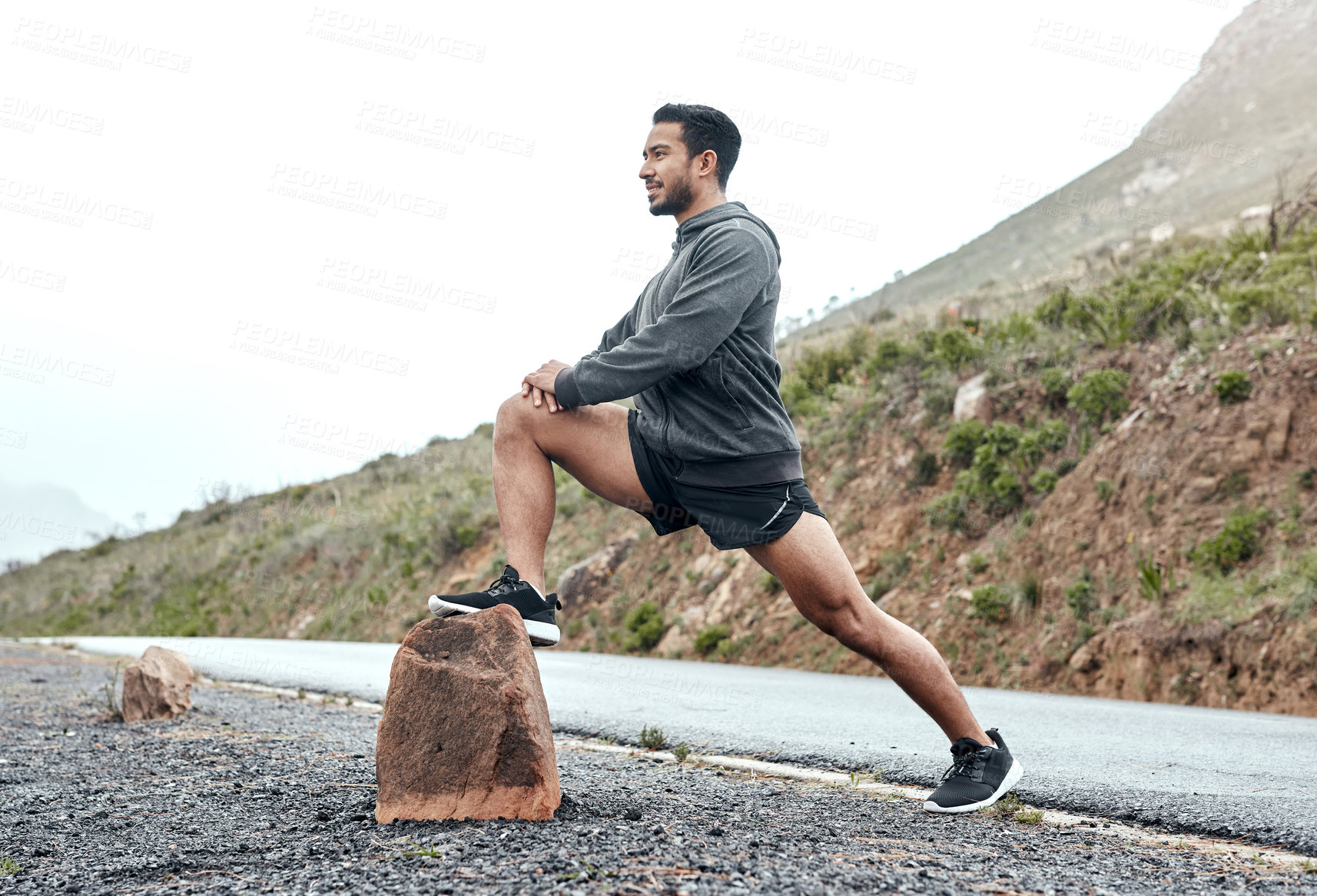 Buy stock photo Shot of a sporty young man stretching his legs while exercising outdoors