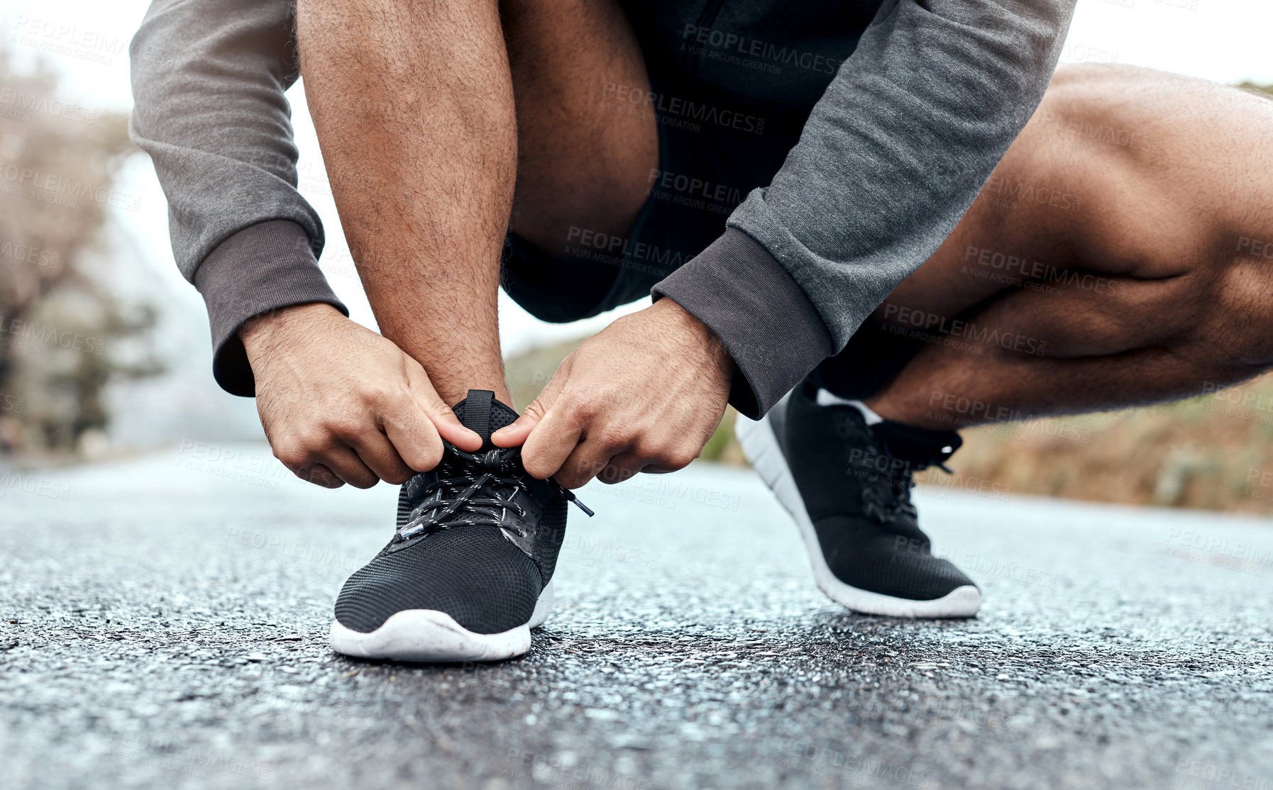 Buy stock photo Closeup shot of an unrecognisable man tying his shoelaces while exercising outdoors