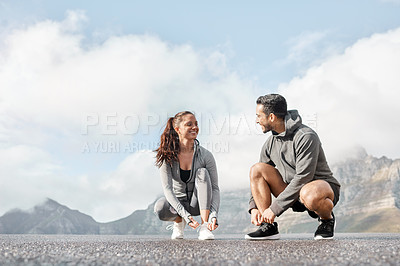 Buy stock photo Shot of a sporty young man and woman tying their shoelaces while exercising outdoors