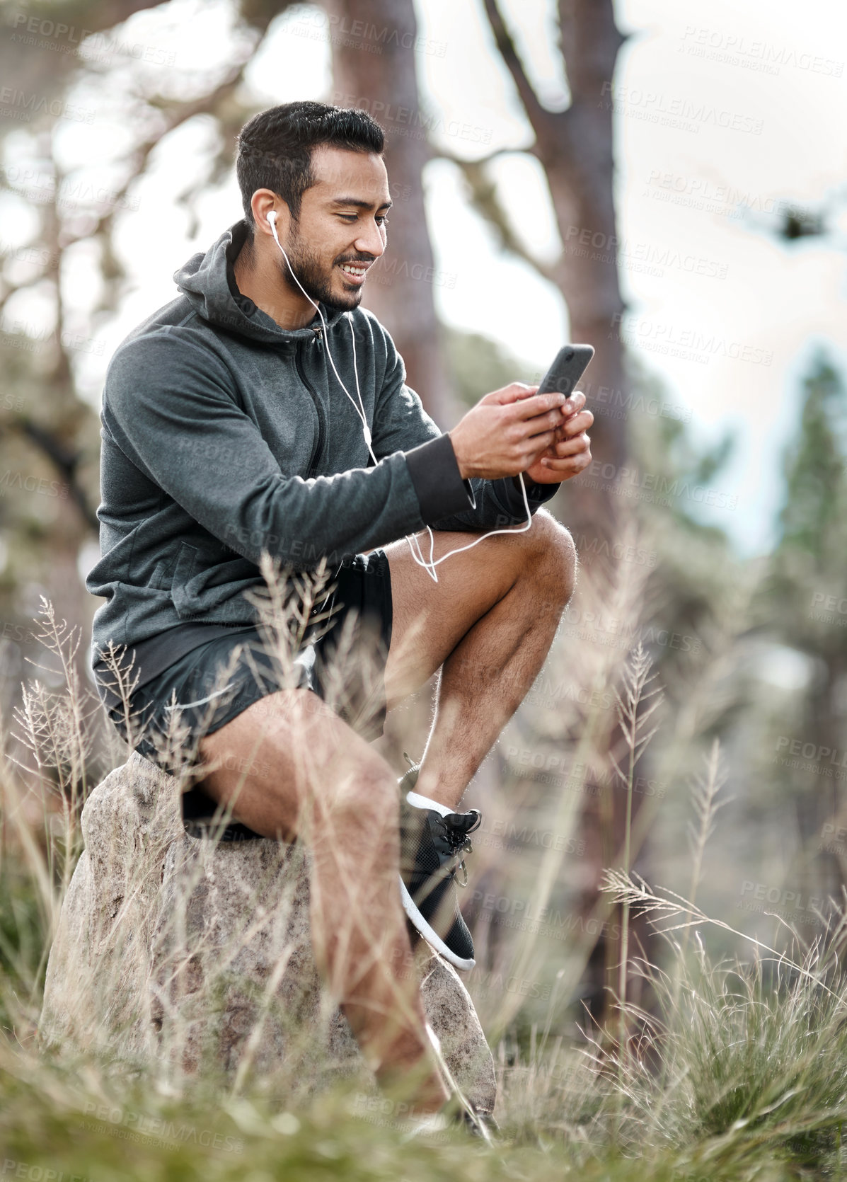 Buy stock photo Shot of a sporty young man wearing earphones while using a cellphone outdoors