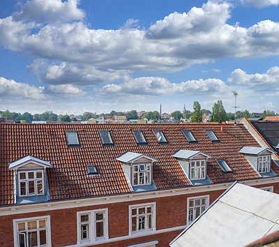 Buy stock photo Rooftop view of buildings in a town with glass windows and frames under a cloudy blue sky. Beautiful landscape architecture with clouds surrounding a suburban urban environment.