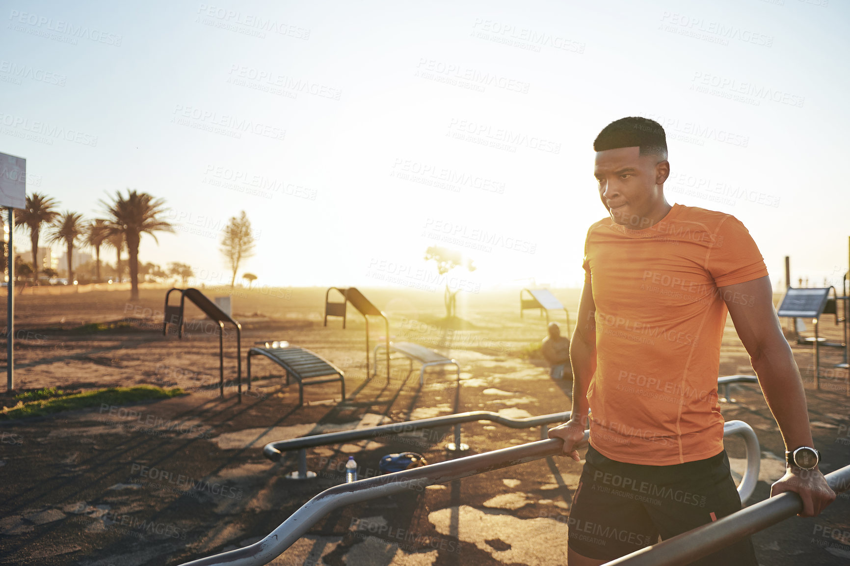 Buy stock photo Shot of a young man working out at the outdoor gym at the park