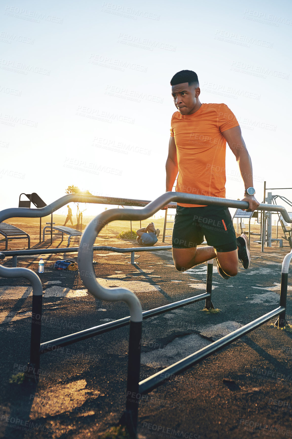 Buy stock photo Shot of a young man working out at the outdoor gym at the park