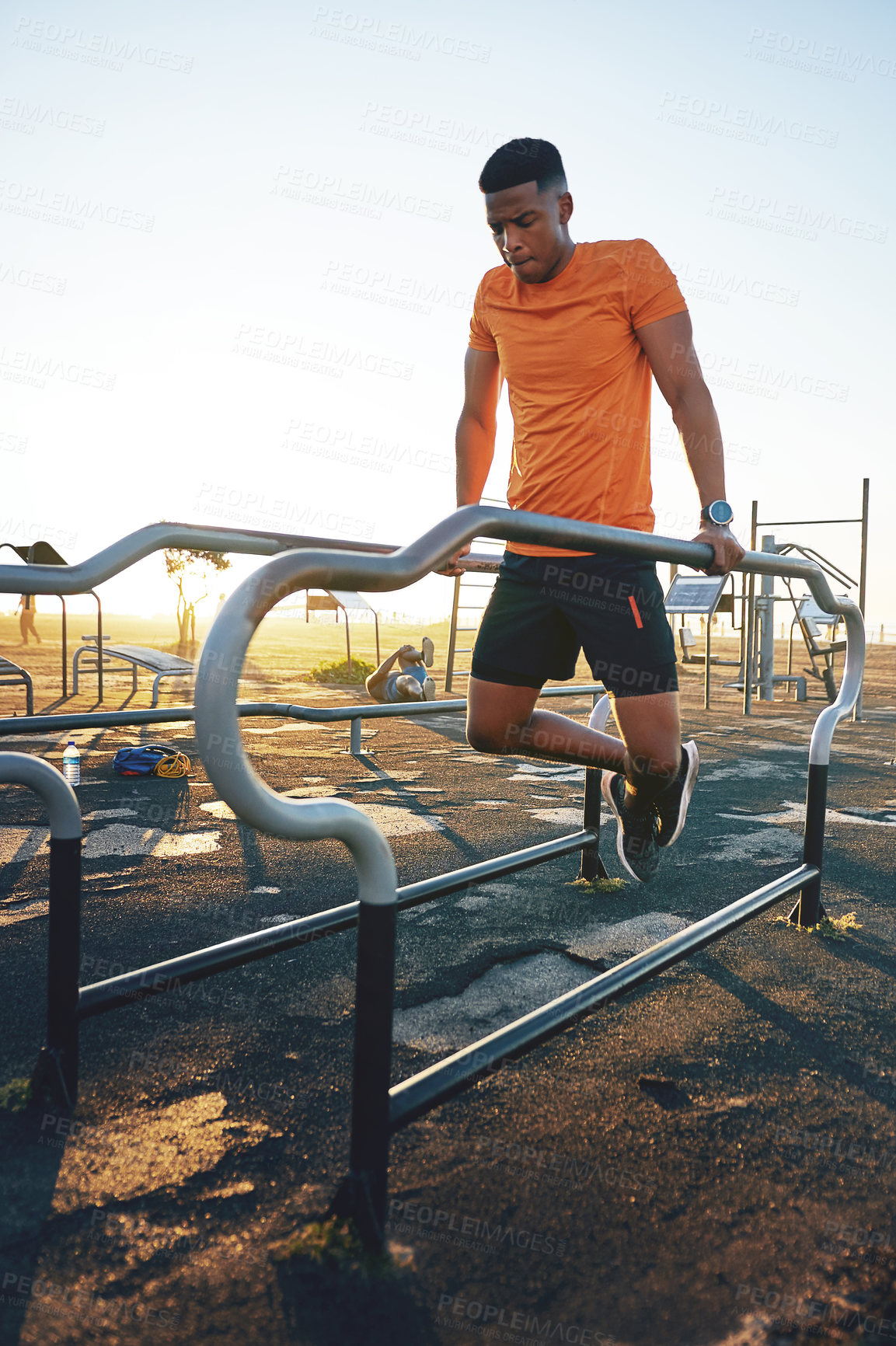 Buy stock photo Shot of a young man working out at the outdoor gym at the park