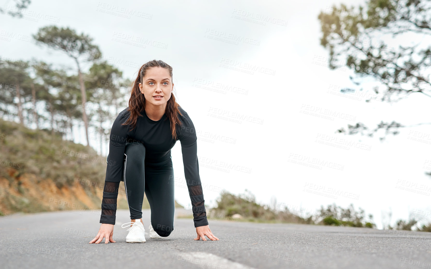 Buy stock photo Full length shot of an attractive young woman crouched down in a starters position before exercising outside