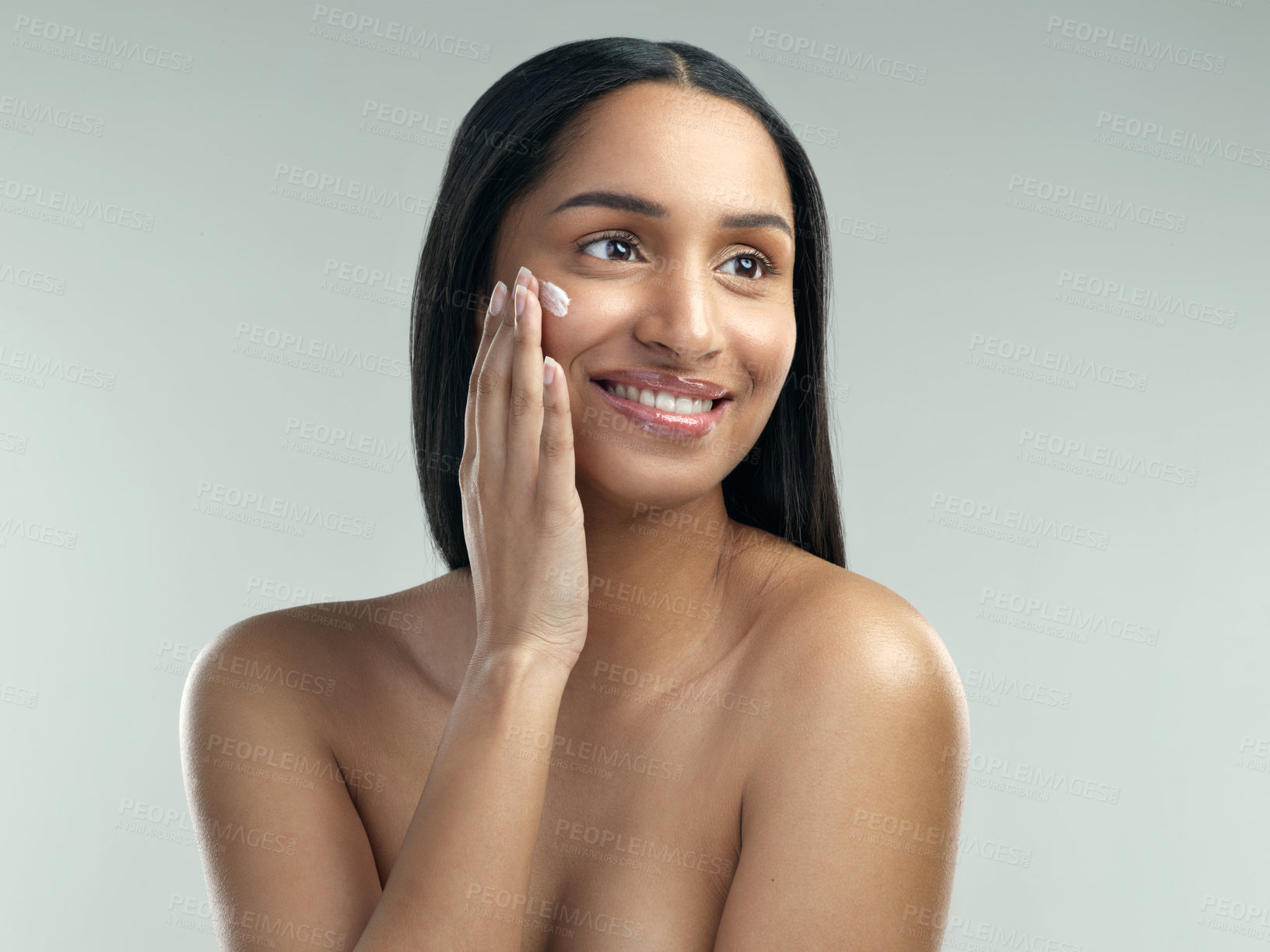 Buy stock photo Shot of a beautiful young woman applying moisturiser to her skin