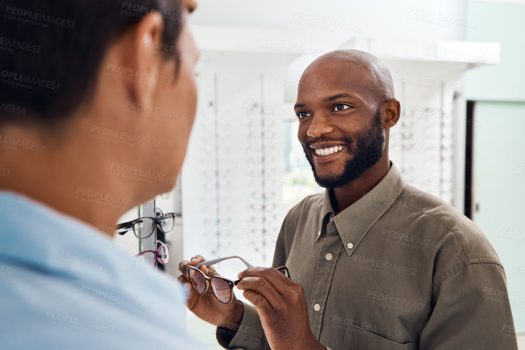 Buy stock photo Shopping for glasses at an optician retail store with a smiling man trying to search for a pair. Optometrist and customer service employee selling a happy buying client new and modern spectacles   
