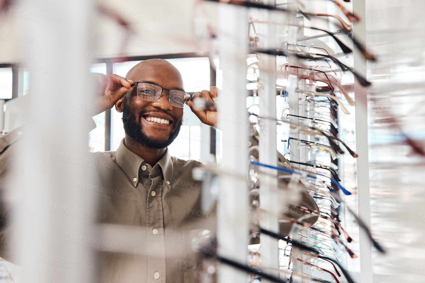 Buy stock photo Shot of a young man buying a new pair of glasses at an optometrist store