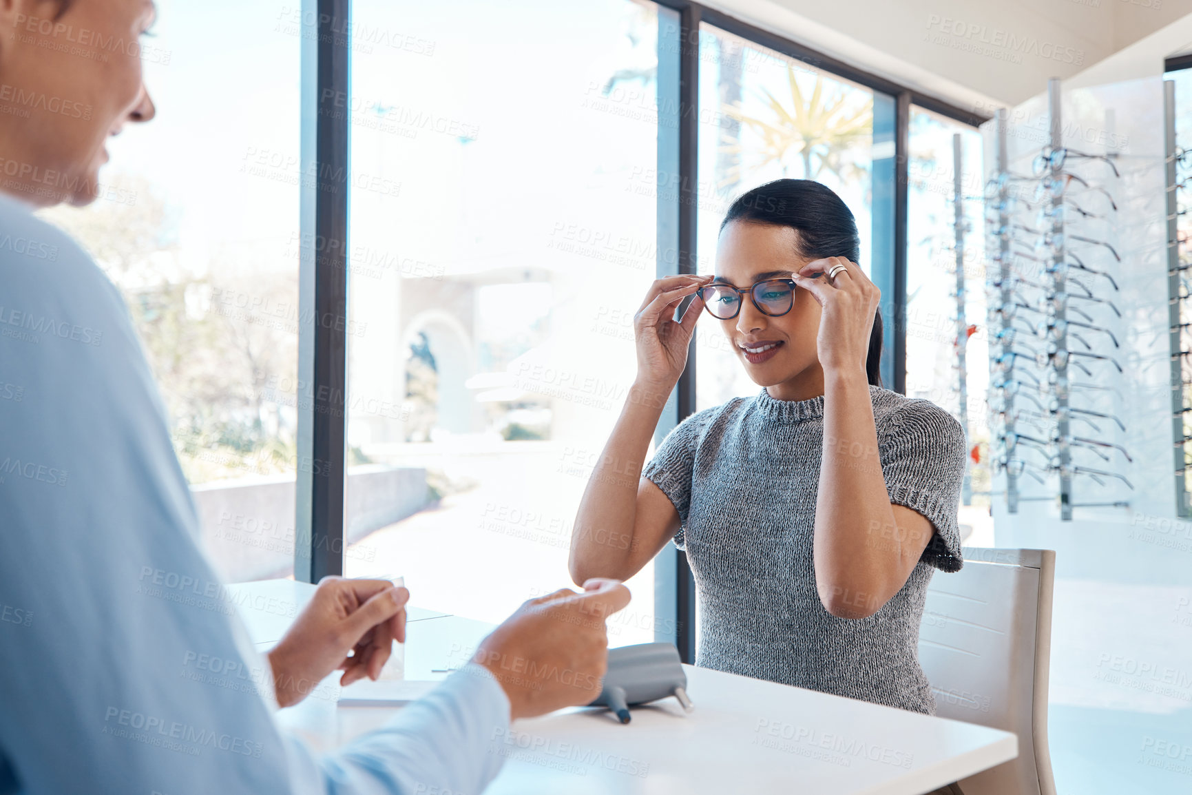 Buy stock photo Shot of a an optometrist helping a young woman choose a new pair of glasses