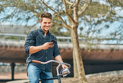 Buy stock photo Shot of a young male student using his mobile phone while cycling on campus