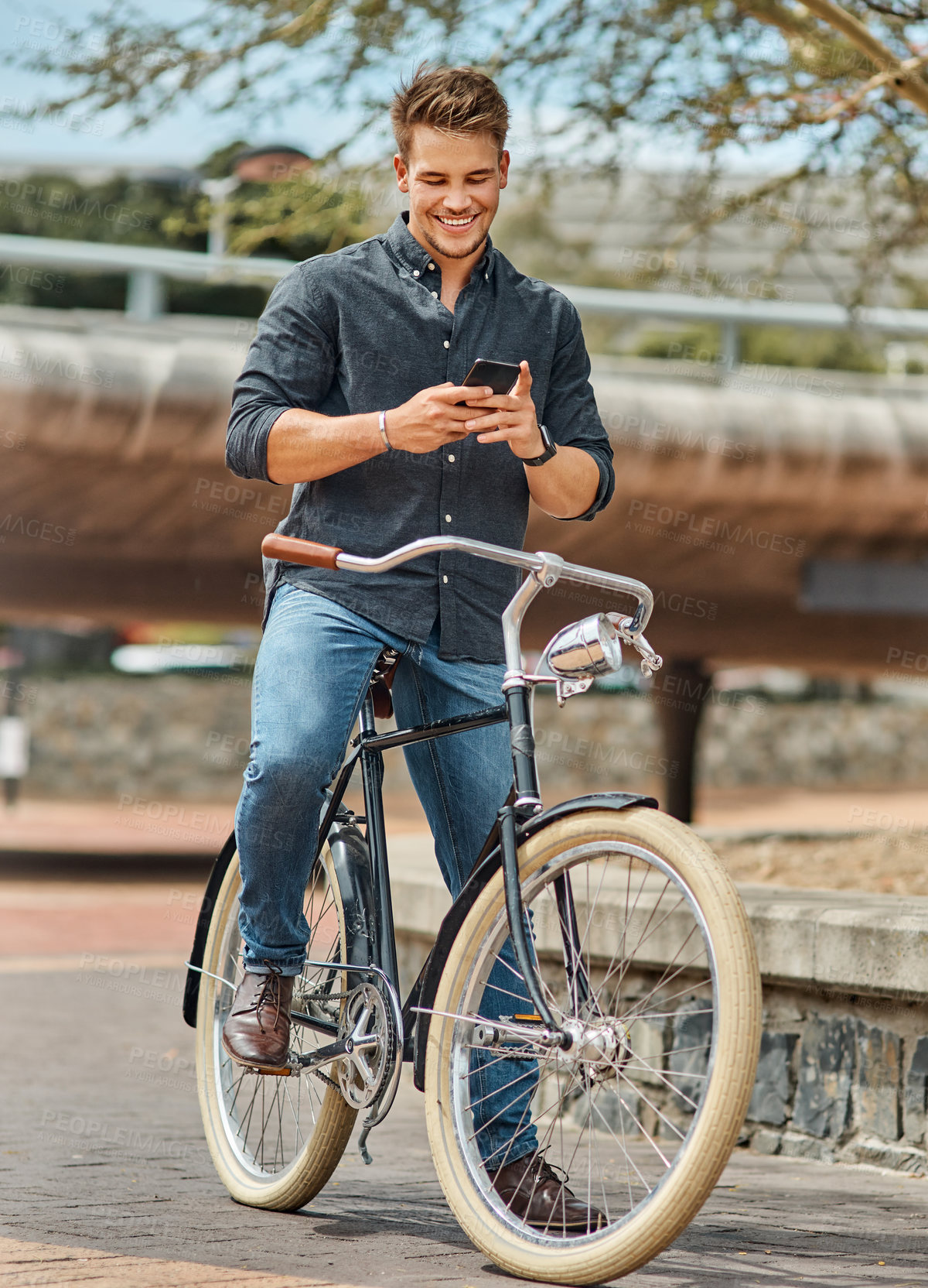 Buy stock photo Shot of a young male student using his mobile phone while cycling on campus