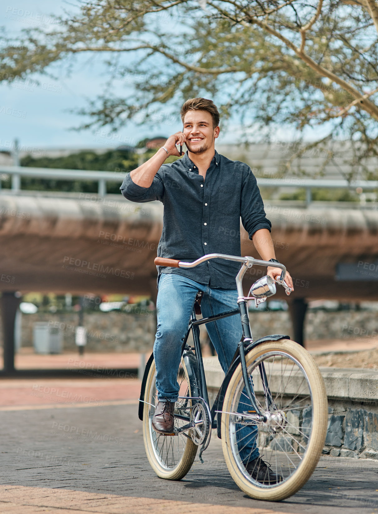 Buy stock photo Shot of a young male student using his mobile phone while cycling on campus