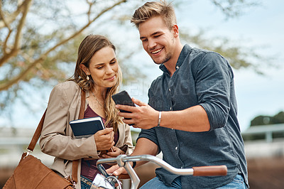 Buy stock photo Shot of two young students using a mobile phone outside on campus
