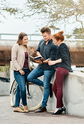 Buy stock photo Shot of a group of young students reviewing a notebook on outside campus