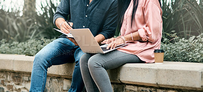 Buy stock photo Shot of two unrecognizable students using a laptop while sitting outside on campus