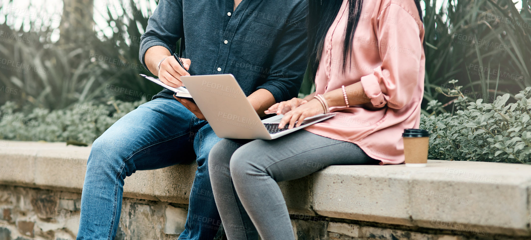 Buy stock photo Shot of two unrecognizable students using a laptop while sitting outside on campus