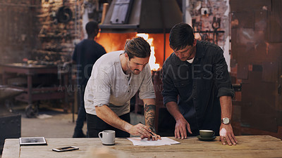 Buy stock photo Shot of two men discussing paperwork while standing together in a workshop