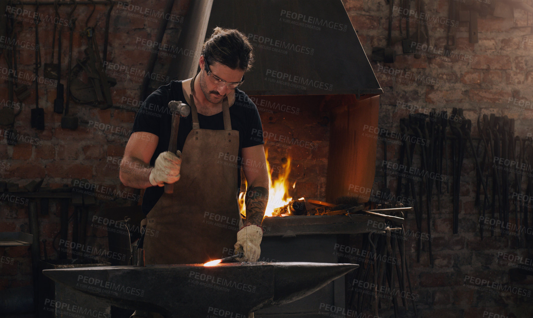 Buy stock photo Hammer, anvil and fire with a man working in a foundry for metal work manufacturing or production. Industry, welding and trade with a young male blacksmith in a workshop, plant or industrial forge