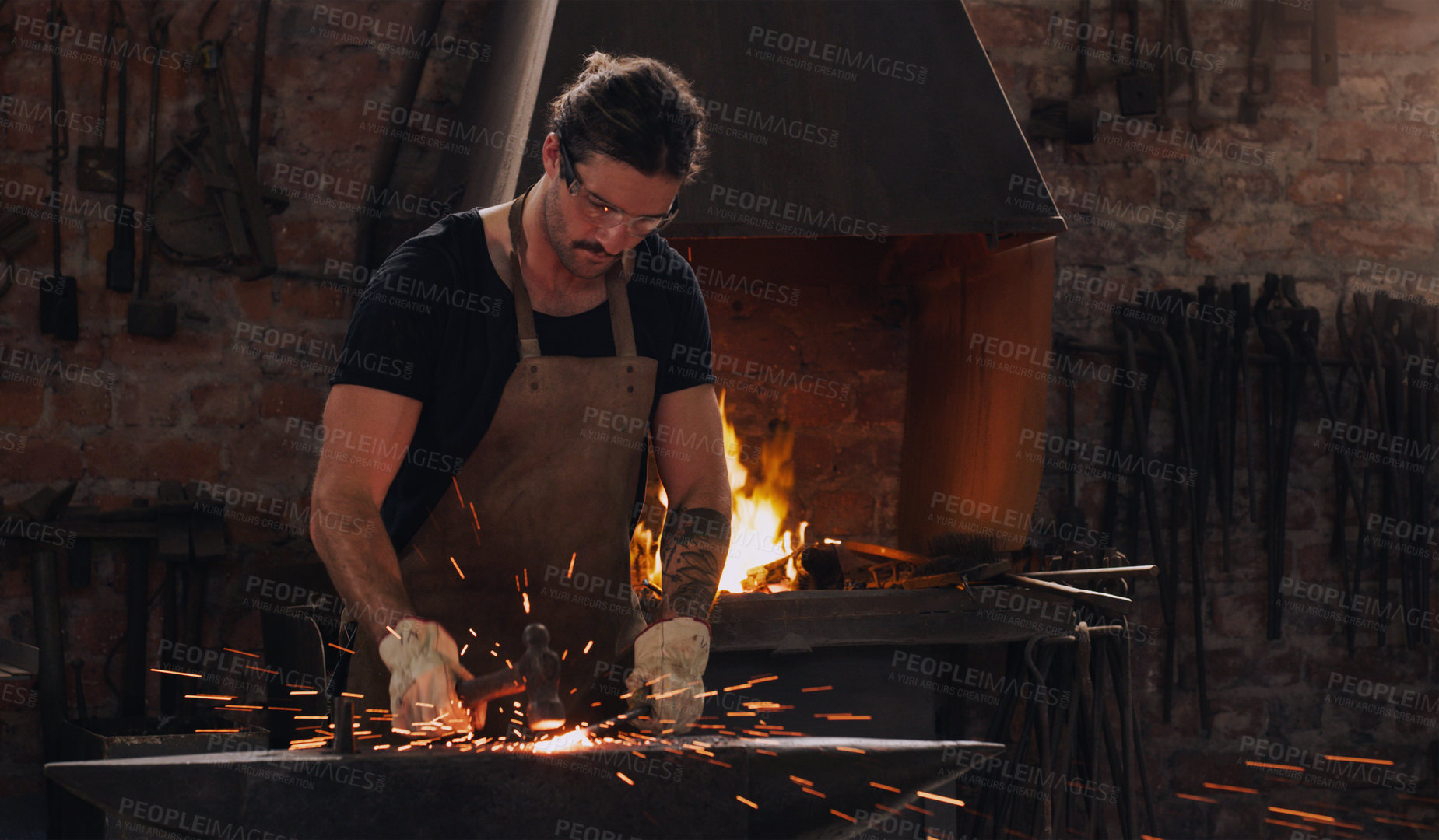 Buy stock photo Hammer, anvil and fire with a man working in a forge for metal work manufacturing or production. Industry, welding and trade with a male blacksmith at work in a factory, plant or industrial workshop