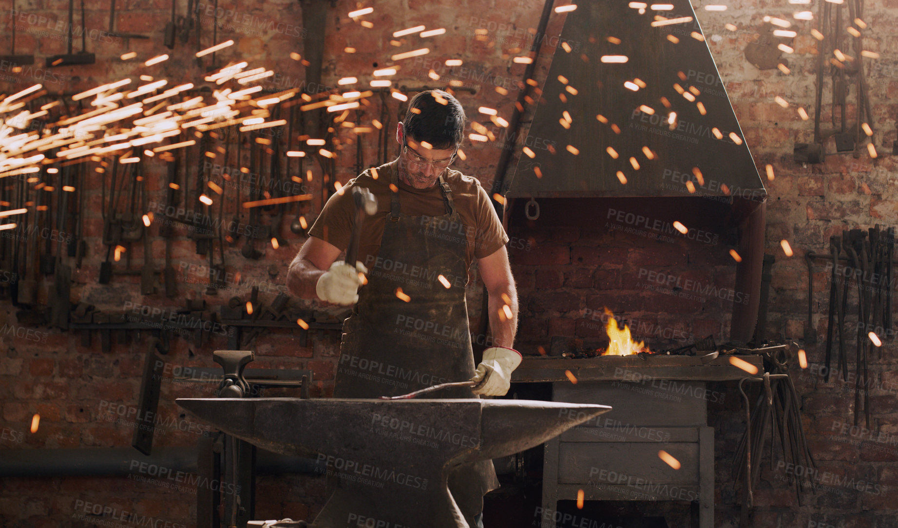 Buy stock photo Hammer, anvil and fire with a man in a forge workshop for metal work manufacturing or production. Industry, welding and trade with a male blacksmith at work in a factory, plant or industrial foundry