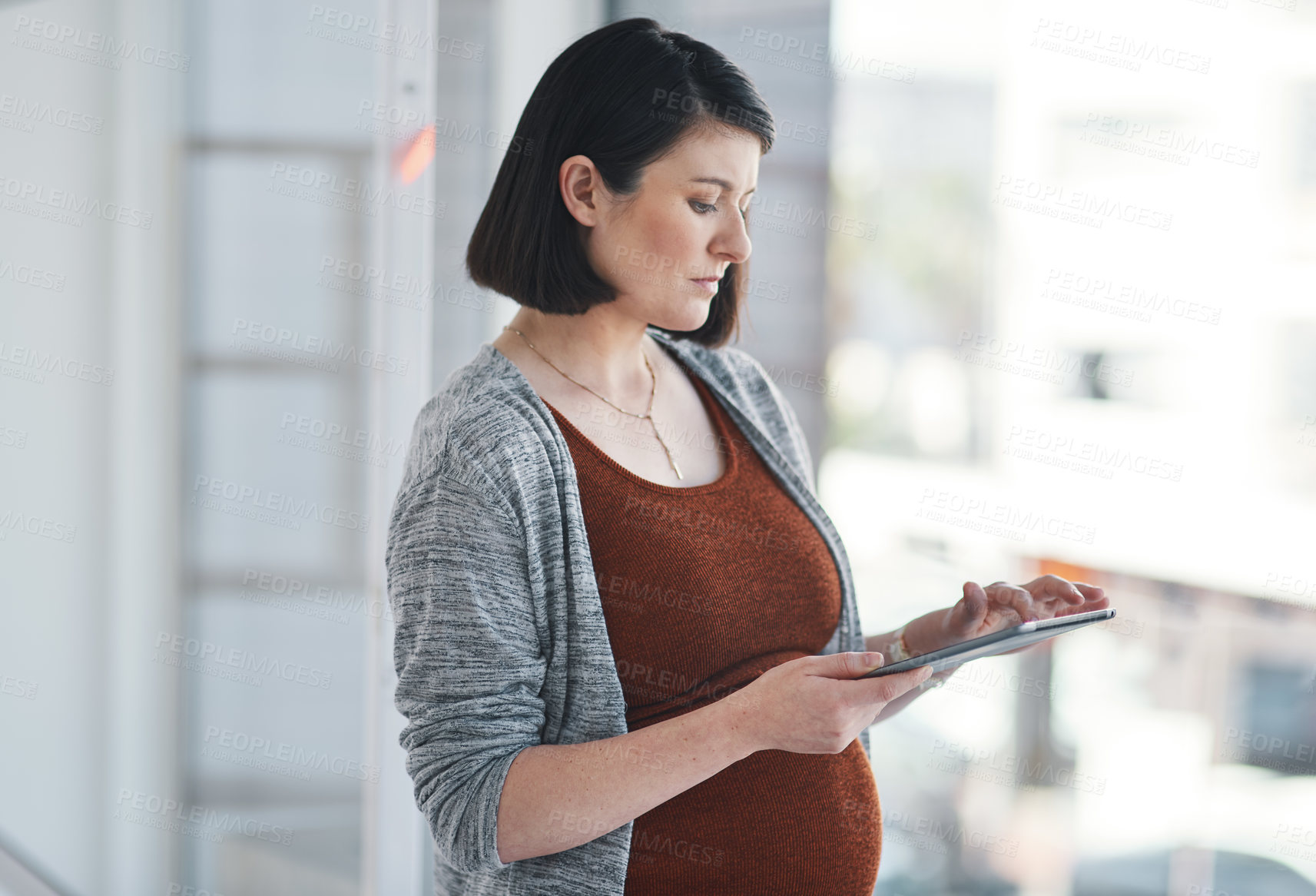 Buy stock photo Shot of a pregnant young businesswoman using a digital tablet in a modern office