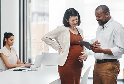 Buy stock photo Shot of a pregnant young businesswoman using a digital tablet during a meeting with her colleague in a modern office