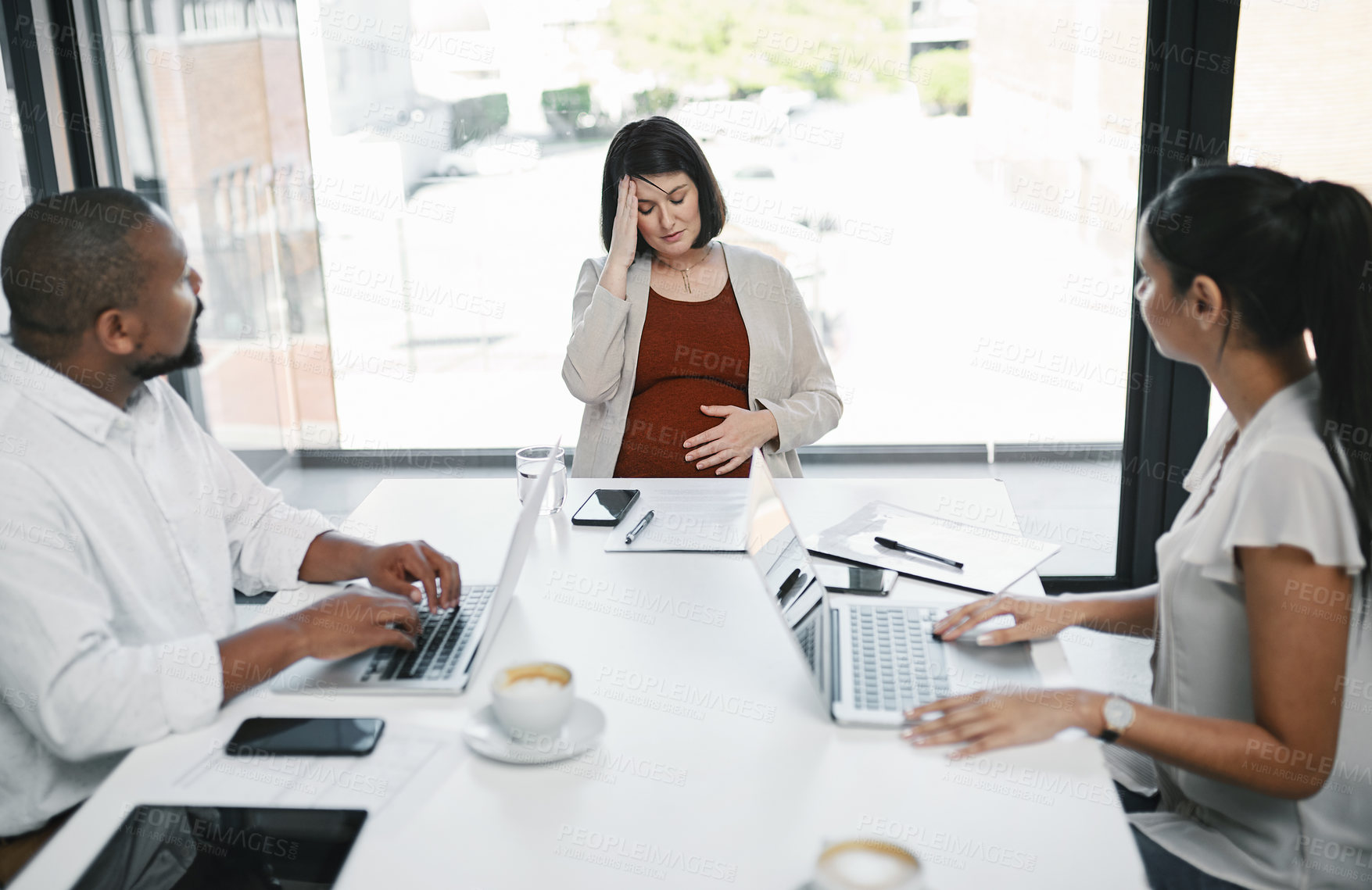 Buy stock photo Shot of a pregnant young businesswoman feeling stressed during a team meeting in a modern office