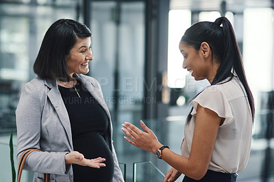 Buy stock photo Shot of a pregnant young businesswoman chatting with her colleague in a modern office