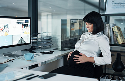 Buy stock photo Cropped shot of an attractive pregnant businesswoman sitting alone in the office and holding her stomach