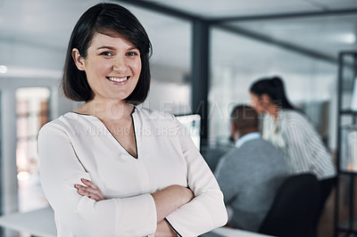 Buy stock photo Cropped shot of an attractive young businesswoman standing with her arms folded while colleagues works behind her