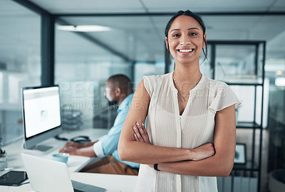 Buy stock photo Cropped shot of an attractive young businesswoman standing with her arms folded while a colleague works behind her