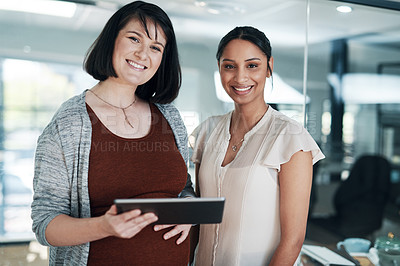 Buy stock photo Cropped shot of two young businesswomen standing together in the office and using a tablet