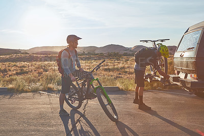 Buy stock photo Full length shot of two young male athletes mountain biking in the wilderness