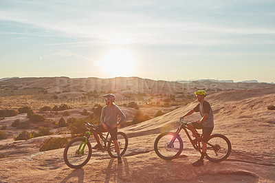 Buy stock photo Full length shot of two young male athletes mountain biking in the wilderness